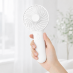 White FS110 handheld fan held in one hand with a compact portable design