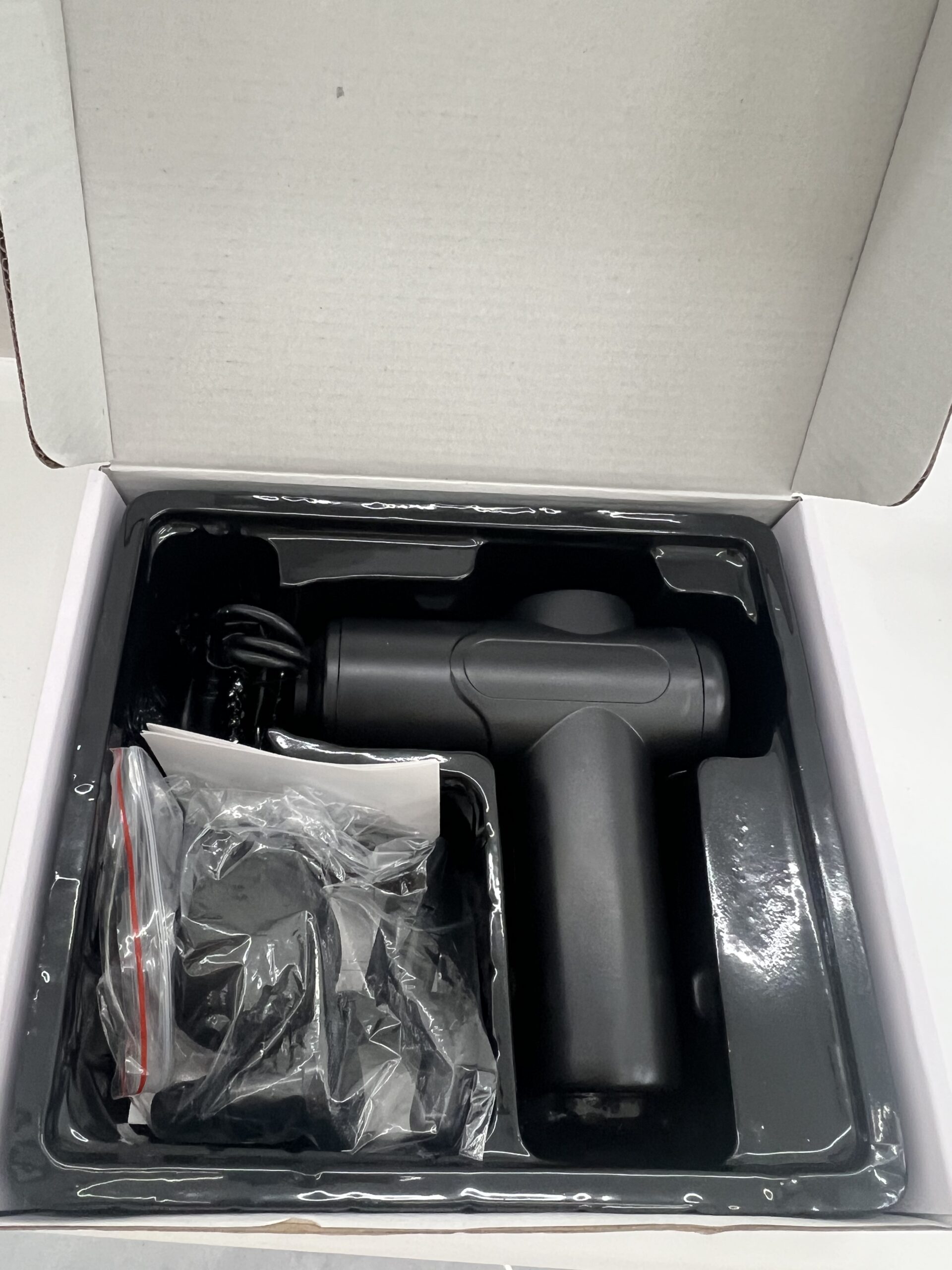 Black mini massage gun arranged inside its retail packaging
